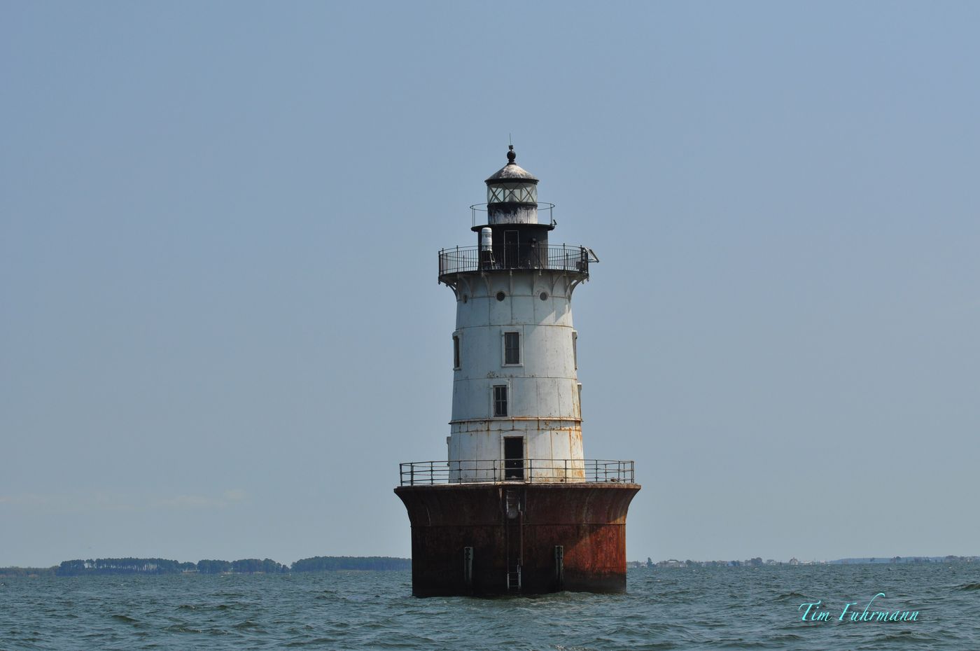The Hooper Island Lighthouse, a white cast-iron tower on a rust-red caisson, standing in the Chesapeake Bay
