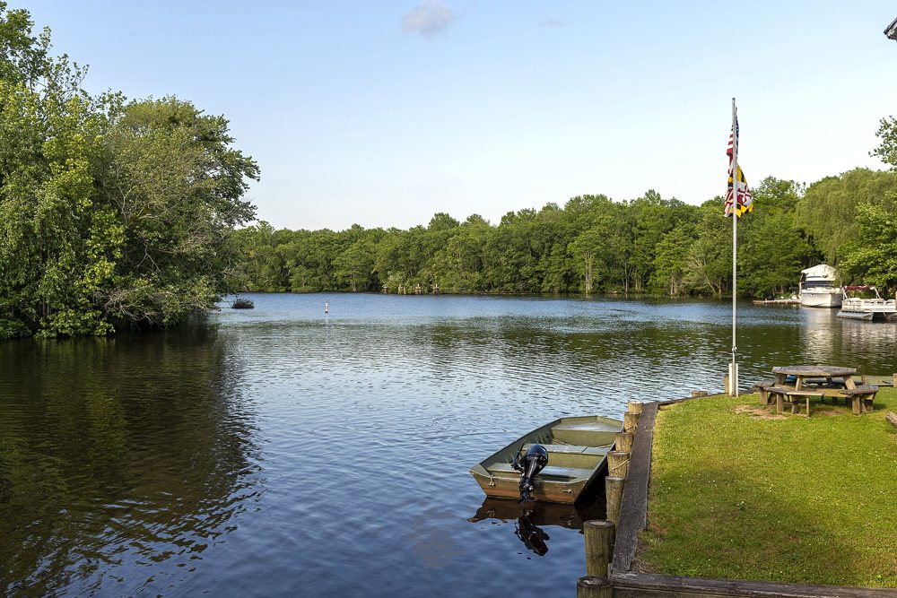 The tree-lined Pocomoke River at Snow Hill, Maryland, with a small boat, picnic table and flagpole on the bank